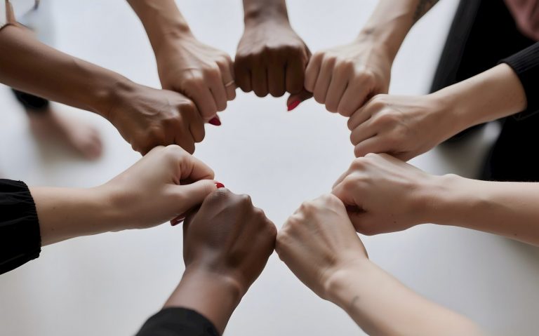 People of diverse skin tones fist bumping in a circle.